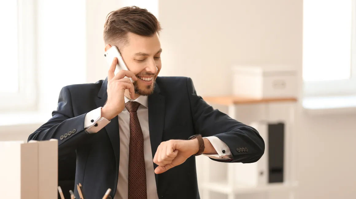 Biznesmen w garniturze, siedzący w biurze, rozmawiający przez telefon i patrzący na zegarek